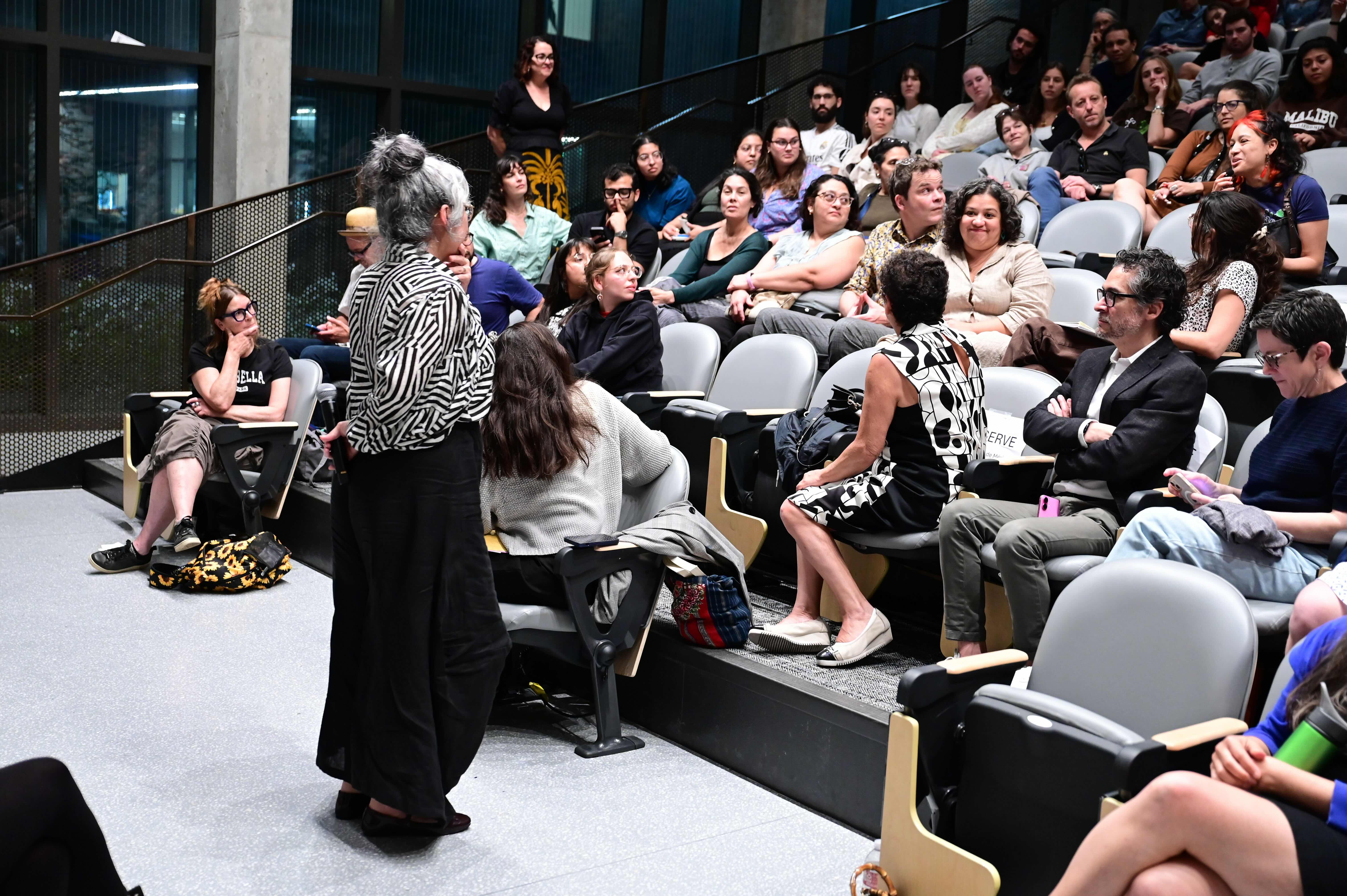 Speaker addresses a diverse audience in a tiered lecture hall.