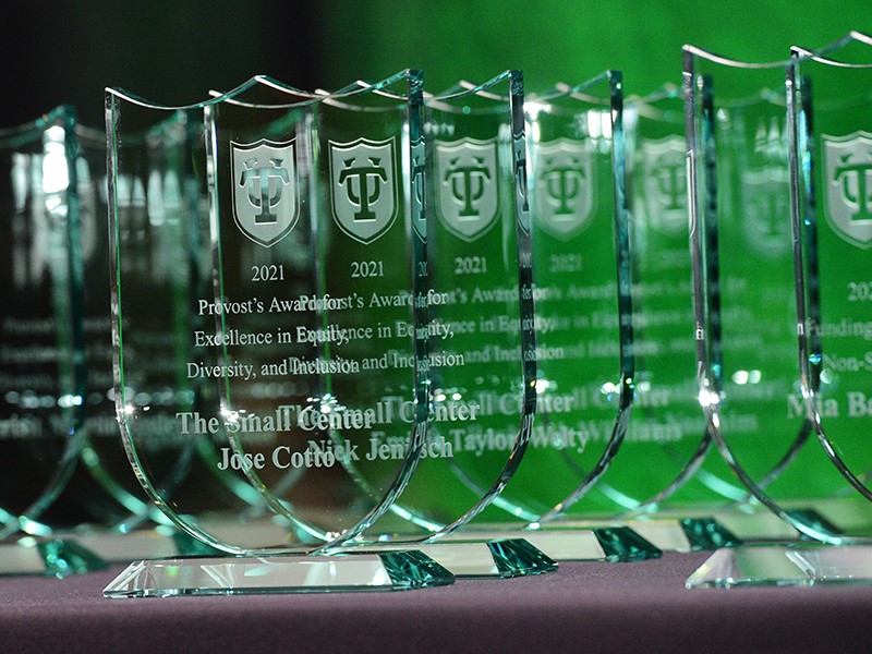 Image of clear glass awards shaped like badges with the names of the winners on them, displayed on a table. 
