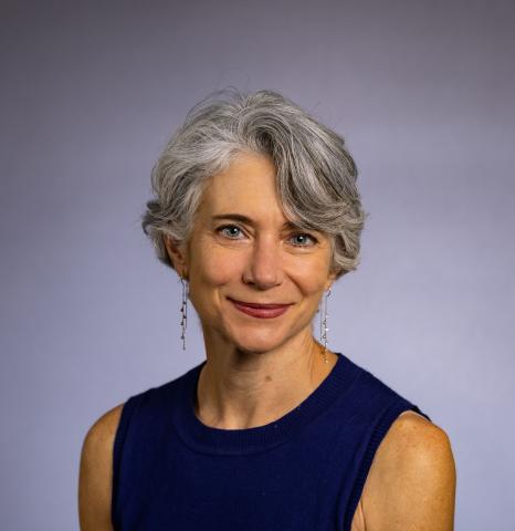 A woman with short, gray hair poses in front of a gradient background.