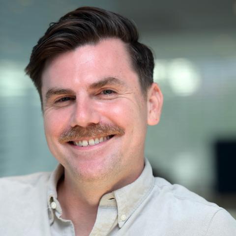 A man with a moustache smiles for the camera.