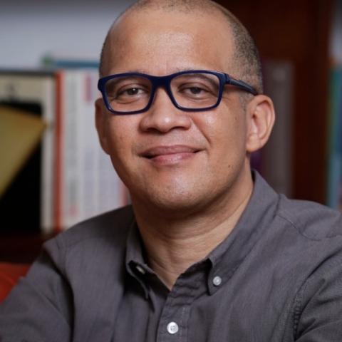 A bald man with glasses and a grey shirt.