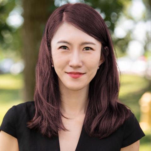 Sina Lee, a woman with dark red hair and a black top, smiles for the camera.