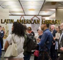 Image of people standing in the Latin American Library, taken through the glass door which reads "Latin American Library," in gold font