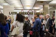 Image of people standing in the Latin American Library, taken through the glass door which reads "Latin American Library," in gold font