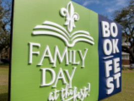 Large green and blue sign for "FAMILY DAY at the fest!" and "BOOK FEST" with a fleur-de-lis graphic.